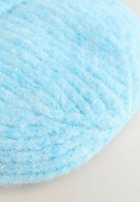 Lyseblå rund strikket pude med en fluffy tekstur og et fletmønster, der har bløde, løse fibre for komfort.