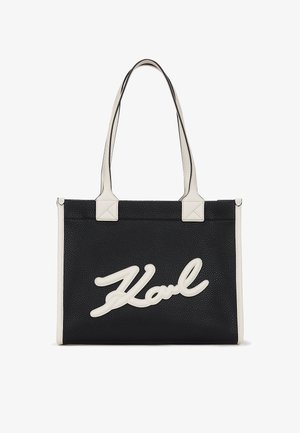 Svart teksturert lær tote-veske med kremfargede detaljer, som har et fremtredende hvitt signaturlogo. To topphåndtak og rektangulær form.