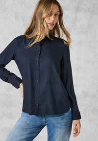Camicetta a maniche lunghe blu navy con bottoni frontali, tessuto morbido e vestibilità leggermente rilassata con orlo curvo.