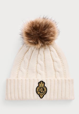 Beanie a maglia crema con motivo a treccia, grande pom-pom in pelliccia marrone sopra, e patch del logo Ralph Lauren in nero e oro sul risvolto.