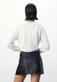 Lichtgrijze sweater met lange mouwen, gecombineerd met een zwarte rok van nepleer met achterzakken en een aansluitend ontwerp.