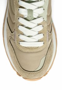 Zapatilla beige con parte superior de ante y nailon, cordones blancos, acentos en verde claro y una suela intermedia texturizada. Presenta un patrón ondulado distintivo.