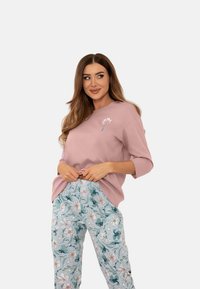 Jasnoróżowy sweter z rękawami do trzech czwartej, zdobiony haftowanym kwiatem. Połączony z spodniami w kwiatowy wzór w pastelowym niebieskim kolorze.