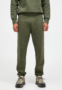 Olivengrønne sweatpants med en afslappet pasform, ribbede manchetter og en glat tekstur. Kombineret med robuste, flerfarvede sneakers.