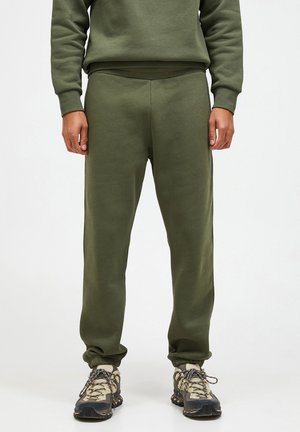 Olivengroene sweatpants met een ontspannen pasvorm, ribbelmanchetten en een gladde textuur. Gecombineerd met robuuste, multikleurige sneakers.
