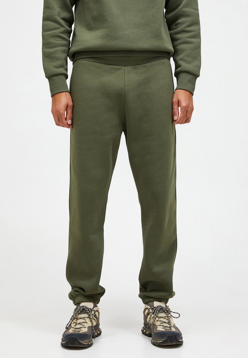 Olivengrønne sweatpants med en afslappet pasform, ribbede manchetter og en glat tekstur. Kombineret med robuste, flerfarvede sneakers.