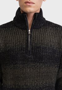 Suéter de punto en verde oscuro y negro, con un cuello alto y media cremallera. La textura es acanalada con un patrón en degradado.