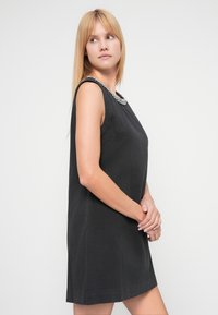 Rochie neagră fără mâneci, cu decolteu rotund și guler brodat cu mărgele, realizată dintr-un material texturat, cu croială largă și siluetă dreaptă.