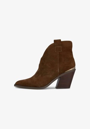 Bottines en daim marron à bout pointu, avec des détails de coutures surélevées et un talon chunky et effilé. Accent métallique sur le talon ajoute un contraste.