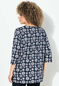 Marineblaues Langarmshirt mit einem sich wiederholenden Schneeflockenmuster in Weiß, Grau und Lila. Weicher Stoff mit lockerer Passform und rundem Ausschnitt.