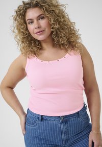 Roza rebrasta majica bez rukava sa izrezom u obliku jaja, s detaljima od zlatnih zakovica duž ruba, u kombinaciji sa plavim farmerkama sa visokim strukom i prugicama.