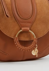 Brun læderhåndtaske med en ruskindsfinish, med et flettet håndtag, en detalje i guldring og en lille nøglecharme.