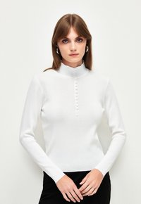Witte lange mouwen top met een hoge kraag, voorzien van een knoopsluiting aan de voorkant en een aansluitend ontwerp, gemaakt van een zachte, gestructureerde stof.