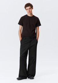 Camiseta de algodón negra y pantalones negros de corte holgado. La camiseta tiene un cuello redondo y los pantalones presentan un diseño de pierna recta.