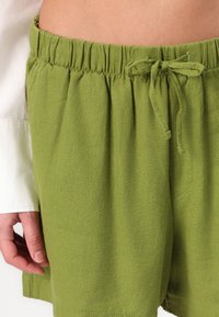 Shorts de lino verdes con cinturilla elástica y lazo ajustable, que presentan un diseño casual y un detalle de bolsillo lateral.