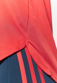 Tejido atlético rojo con una superficie texturizada, que presenta un dobladillo curvado y pantalones navy con rayas rojas verticales en los laterales.