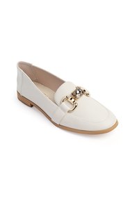 Zapatos planos de cuero blanco con puntera redondeada, que cuentan con un acento de hardware dorado y un detalle decorativo de piedra en la parte superior. Suela marrón clara.