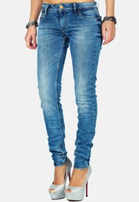 Jeans skinny in denim blu con una finitura sbiadita, caratterizzati da cinque tasche, cuciture in vista e vita media, abbinati a tacchi argentati lucidi.