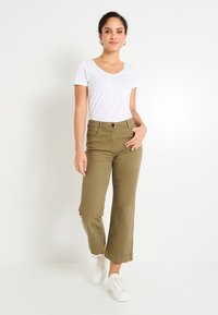 Pantalones de pierna ancha verde oliva con cintura alta, cierre de botón y bolsillos laterales; combinados con una camiseta blanca de escote en V y zapatillas blancas.