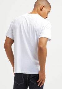 Hvid kortærmet t-shirt med rund hals, glat tekstur og en afslappet pasform, vist bagfra mod en ensfarvet baggrund.