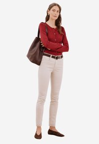 Maglietta rossa a maniche lunghe con bottoni, jeans skinny beige, cintura marrone, grande borsa tote marrone scuro e ballerine marroni con borchie.
