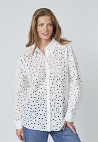 Hvid langærmet skjorte lavet af broderet bomuldsstof med udskårne blomster mønstre, med knaplukning foran og krave.