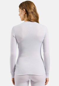 Long-sleeve thermal top in white, featuring ribbed texture, fitted design, and side slits at the hem. Soft and breathable material.
