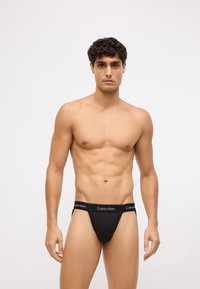 Czarny bawełniany string z szerokim elastycznym paskiem z logo "Calvin Klein". Dopasowany fason i gładka faktura.