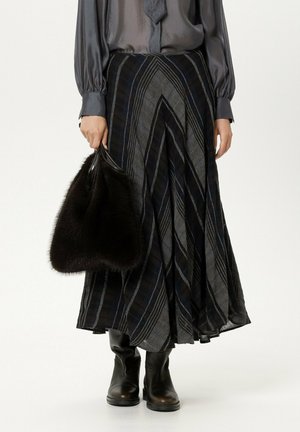 Person trägt eine graue Bluse, einen langen schwarz-grau gestreiften Rock, schwarze Stiefel und hält eine schwarze pelzige Handtasche.