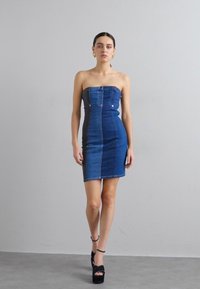 Šaty z denimu bez ramínek s přiléhavým střihem, obsahující různé odstíny modré, zlaté kovové detaily a rovný lem.