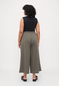 Μαύρη αμάνικη μπλούζα συνδυασμένη με ελαιόπρασινα παντελόνια με φαρδύ πόδι, που διαθέτουν ελαστική μέση. Το μοντέλο φορά μαύρα slipper παπούτσια.