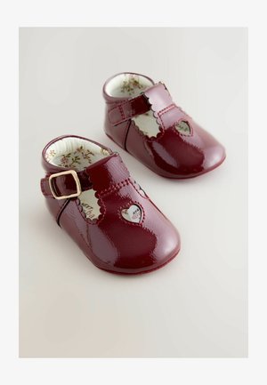 Zapatos de bebé de charol rojo con bordes ondulados, recortes en forma de corazón, hebilla dorada y forro con patrón floral. Diseño de punta redondeada.
