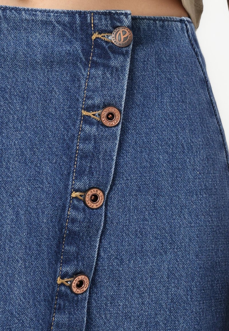 Jeansrock mit einer Vorderknopfverschluss, der sechs kupferfarbene Knöpfe und gelbe Nähte aufweist. Die Textur ist weich, mit einer blauen Waschung.