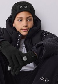 Black puffer jacket with logo detailing, ribbed black beanie, and black gloves with grey fingertips, worn against a neutral background.