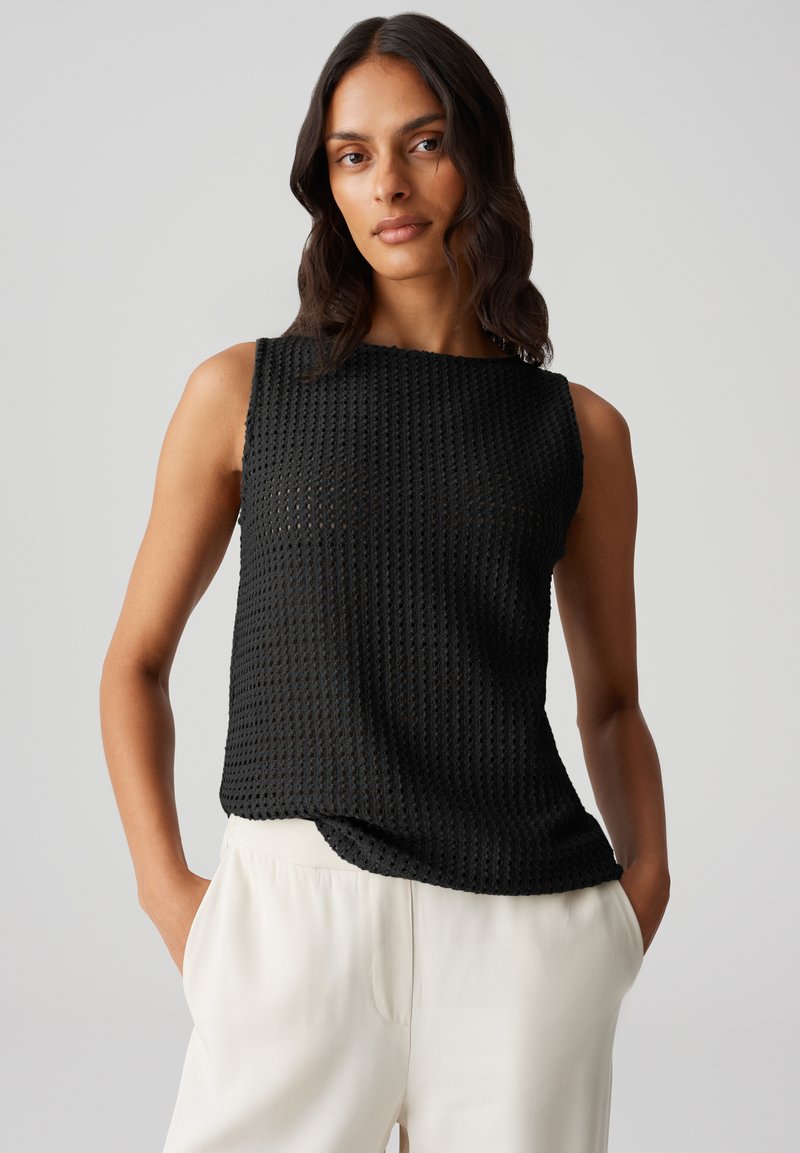 Top nero senza maniche con un design a trama aperta e testurizzata. Collo rotondo e una vestibilità rilassata, abbinato a pantaloni chiari.