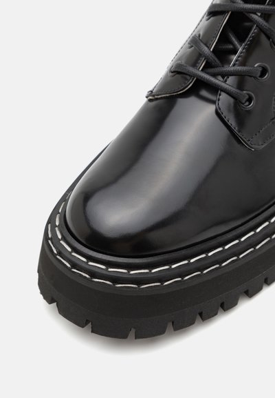 Schwarzer Lederschuh mit hohem Glanzfinish, dicker schwarzer Gummisohle, weißer Naht entlang der Kante und standardmäßiger Schnürdesign.