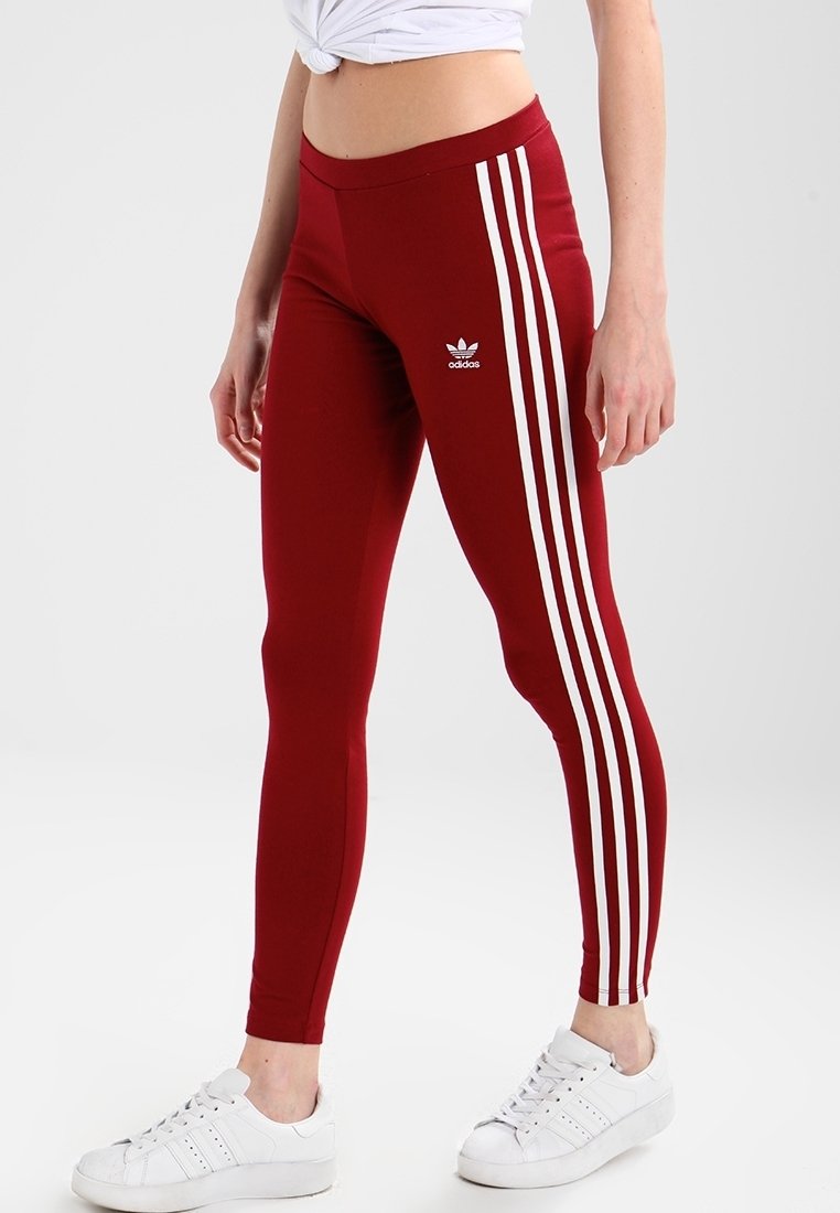 Röda leggings med vita trippla ränder längs sidorna, tillverkade av elastiskt material. Har en Adidas-logga på övre vänstra sidan.