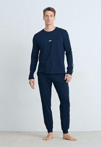 Navy bl� loungewear-set med langermet topp og tettsittende bukser, laget av mykt stoff med minimalistisk design og logo-detaler.