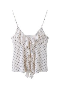 Blouse blanche sans manches avec des pois noirs, fines bretelles, col en V et détail à volants à l'avant noué avec un nœud.