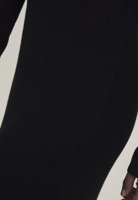 Abito nero in maglia con texture a coste, design aderente e maniche lunghe. Le cuciture sui lati ne migliorano l'aspetto.