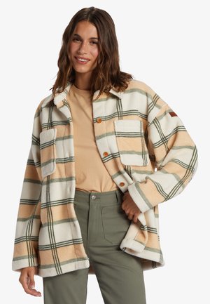 Plaid flannel shirt jacket in cream, peach, and green tones. Features front buttons, two chest pockets, and a relaxed fit. Textured fabric.