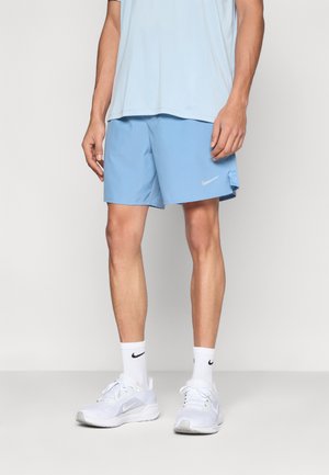 Svetlomodré športové šortky s hladkým textúrou, s malým bielym logom Nike. Nosené s bielymi topánkami a ponožkami.