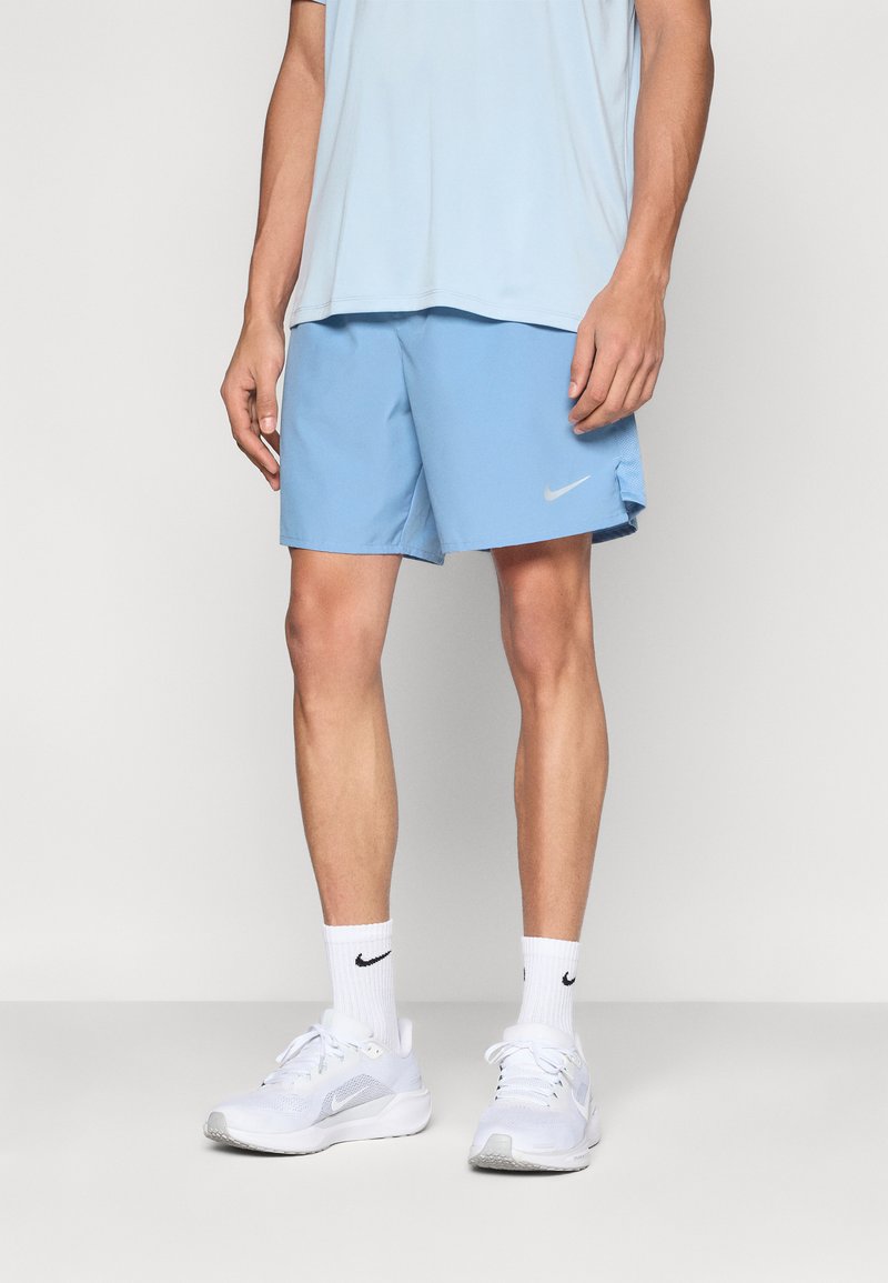 Αθλητικό σορτς σε ανοιχτό μπλε χρώμα με ομαλή υφή, με μικρό λευκό λογότυπο της Nike. Φορώντας λευκά παπούτσια και κάλτσες.
