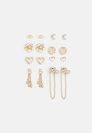 Gold-tone earring set featuring various shapes: flowers, hearts, eyes, moons, and chains; some with clear crystals; mixed designs and textures.