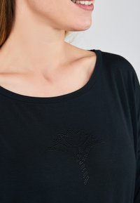 Zwarte T-shirt met een ronde halslijn, voorzien van een strassontwerp van een bladerenpatroon op de voorkant, met een gladde, zachte textuur.