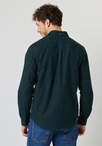 Donkergroen overhemd met lange mouwen van zachte stof, voorzien van een geknoopte kraag, een achterpandnaad en knoopmouwen.