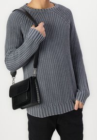 Šedý pletený svetr s texturovaným vzorem a žebrovanými manžetami, doplněný černou kabelkou přes rameno s kroko vzorem a klopovým zapínáním.