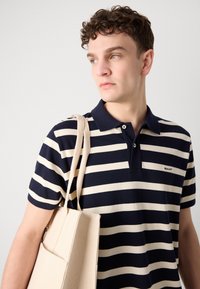 Marineblå og kremfarget stripete polo skjorte med krage og kortermet; parret med en lysebeige kanvas toteveske med sidelomme.