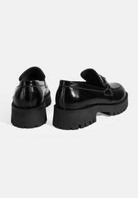 Glanzende zwarte leren schoenen met een stevige zwarte zool en een instapmodel ontwerp. Kenmerkt zich door verhoogde naden en een ronde neus.