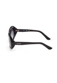 Lunettes de soleil noires à monture œil de chat avec verres teintés foncés, larges branches brillantes et logo "GUESS" sur la branche.